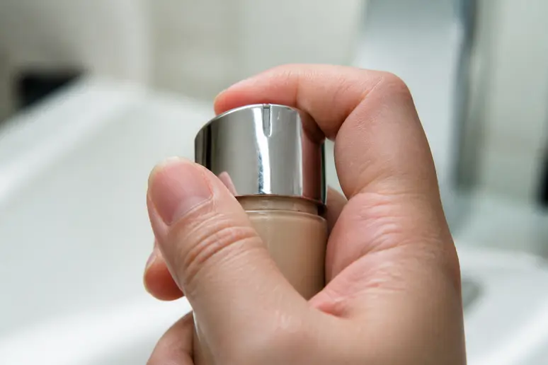 Detail of a hand interacting with a cosmetic product packaging, highlighting a potential flaw.