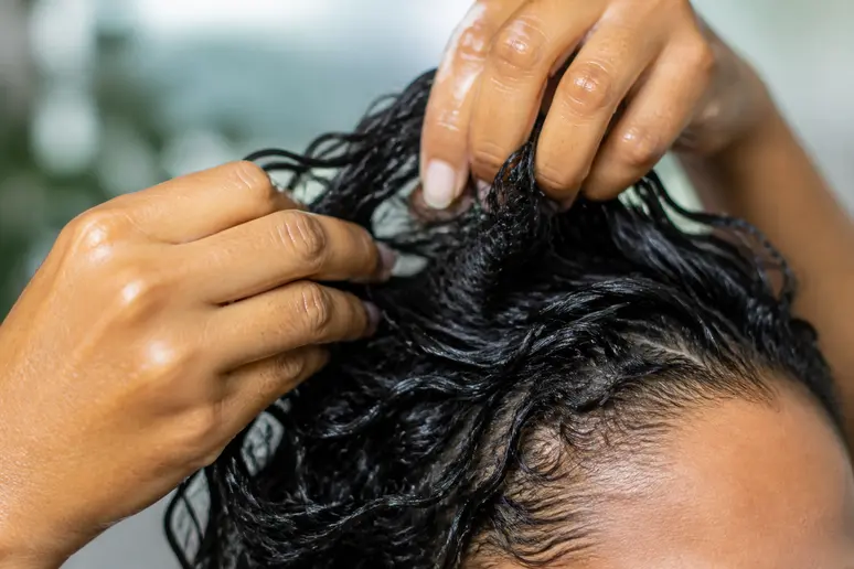 Mains appliquant une noisette de gelée capillaire sur des mèches humides pour définir les boucles