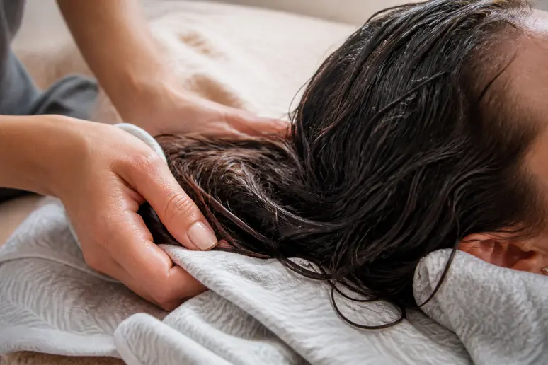 Mains déposant délicatement des cheveux bouclés sur un tissu souple pour une étape de plopping