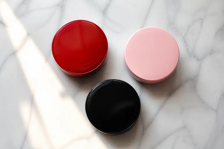 Comparatif des boîtiers de fond de teint Tirtir rouge, rose et noir sur un plan de travail