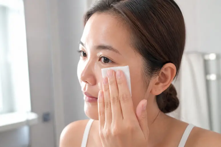 Application délicate d'un toner pad coréen sur le visage propre le matin.