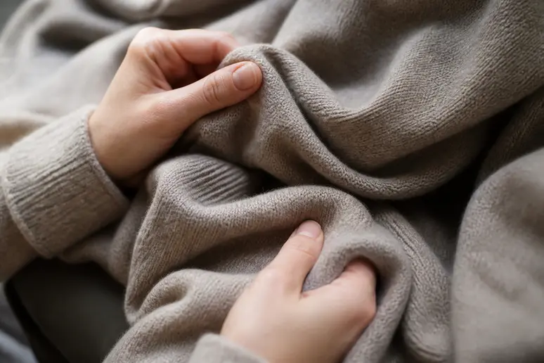 Mains touchant un pull en maille douce pour illustrer les caractéristiques de la collection Peter Hahn