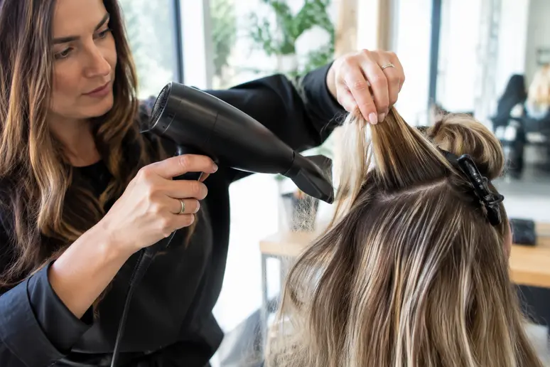 Coiffeur utilisant un sèche-cheveux pour séparer les mèches lors d'un airtouch balayage en salon