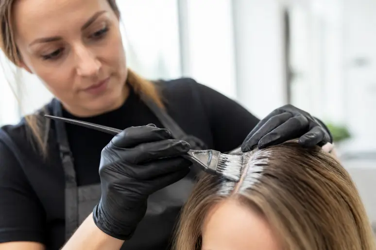 Coiffeur appliquant une coloration sans ammoniaque sur les racines avec un pinceau.