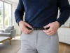 Pantalon qui descend : que faire s’il glisse avec ceinture ? Personne ajustant une ceinture plate sur un pantalon qui descend dans un salon lumineux